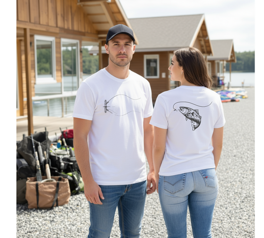 Two people wearing white t-shirts with fish designs, standing outdoors near a wooden cabin.