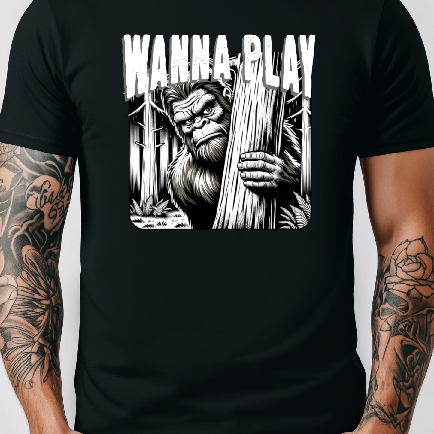 Black t-shirt with creepy Bigfoot design peeking from behind a tree and bold text that reads ‘Wanna Play’ – horror cryptid graphic shirt